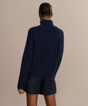 A person with their hair in a bun is shown from behind, wearing the Boyd Cashmere Sweater in dark blue and black shorts against a plain beige background.