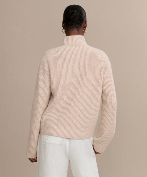 A person with their hair in a bun is shown from the back, wearing the cream Boyd Cashmere Sweater and white pants, standing against a plain beige background.