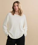 A woman with shoulder-length blonde hair wears an oversized Cashmere Chandler Long-Sleeve Tee with a chest pocket and black pants, standing against a plain beige background.