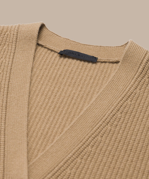 Close-up of the Cashmere Cocoon Cardigan in beige ribbed knit with a V-neckline and a dark label inside the collar, displayed on a neutral background.