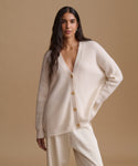 A woman modeling a matching cream-colored knit cardigan and wide-leg trousers set against a solid beige studio background.