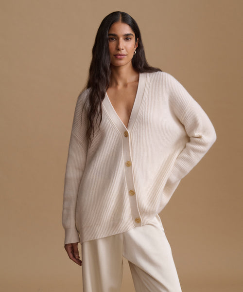 A woman modeling a matching cream-colored knit cardigan and wide-leg trousers set against a solid beige studio background.