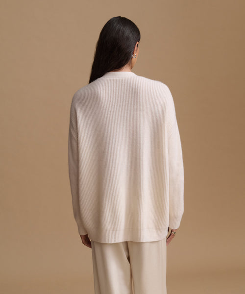 A woman shown from the back wearing a cream-colored ribbed knit sweater and matching cream pants against a solid beige studio background.