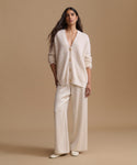 A woman modeling a matching cream-colored knit cardigan and wide-leg trousers set against a solid beige studio background.