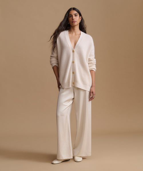 A woman modeling a matching cream-colored knit cardigan and wide-leg trousers set against a solid beige studio background.