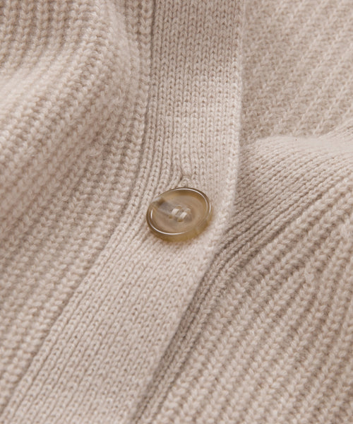 Close-up of the beige knit fabric of the Cashmere Cocoon Cardigan, featuring a single round tan button. The texture and stitching highlight the cardigans softness and detailed craftsmanship.