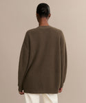 Seen from behind, a person with dark hair in a low bun wears the Cashmere Cocoon Cardigan in ribbed brown with white pants, standing against a plain beige background.