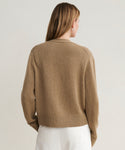 A woman with long, light brown hair is seen from the back, wearing the Cashmere Colette Cardigan and white pants against a neutral background.