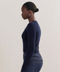 A woman with her hair in a neat bun is shown in profile, wearing the Cashmere Finley Cardigan in dark navy with high-waisted blue jeans, standing against a plain light background.