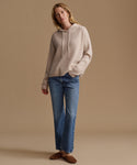 A woman modeling a light beige ribbed knit hoodie and blue jeans against a solid beige studio background.