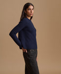 A woman modeling a navy blue ribbed knit sweater with dark charcoal jeans, standing against a solid warm beige studio background.