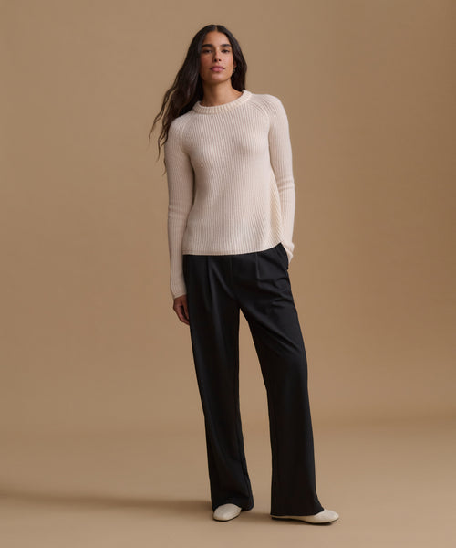 A woman modeling a cream ribbed knit long-sleeve sweater with black wide-leg trousers, standing against a solid beige studio background.