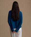 Woman wearing a blue cashmere sweater and white pants against a brown background