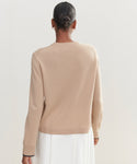 A person with short hair wears the Flynn Cashmere Crewneck in light beige and a white skirt, seen from behind against a plain, light background.