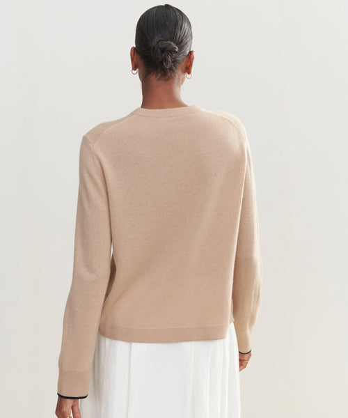 A person with short hair wears the Flynn Cashmere Crewneck in light beige and a white skirt, seen from behind against a plain, light background.
