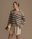 Woman wearing a beige cashmere sweater with black stripes and beige shorts against a brown background