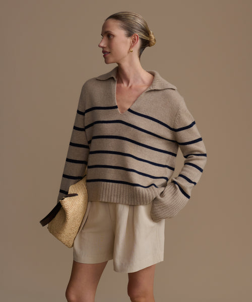 Woman wearing a beige cashmere sweater with black stripes and beige shorts against a brown background