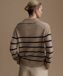 Woman wearing a beige cashmere sweater with black horizontal stripes against a beige background