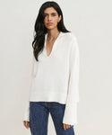 A woman with long dark hair wears the ivory Cashmere Frances Polo, featuring a V-neck, wide sleeves, and relaxed fit, paired with blue jeans against a plain light background.