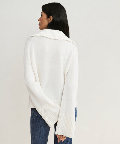 A woman faces away, wearing the ivory Cashmere Frances Polo—a relaxed-fit, long-sleeve knit with wide ribbed cuffs and collar—paired with blue jeans against a plain light background.