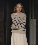 Woman wearing a beige cashmere sweater with blue stripes and a white skirt standing in front of a dark wooden door.