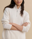 A woman with long brown hair wears the Cashmere Half Zip sweater with sleeves rolled up, standing with her arms crossed against a beige background.