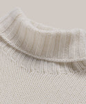 Close-up of the Cashmere Jet Turtleneck, a cream-colored ribbed oversized sweater, showcasing the lightweight knit texture and pattern against a neutral background.