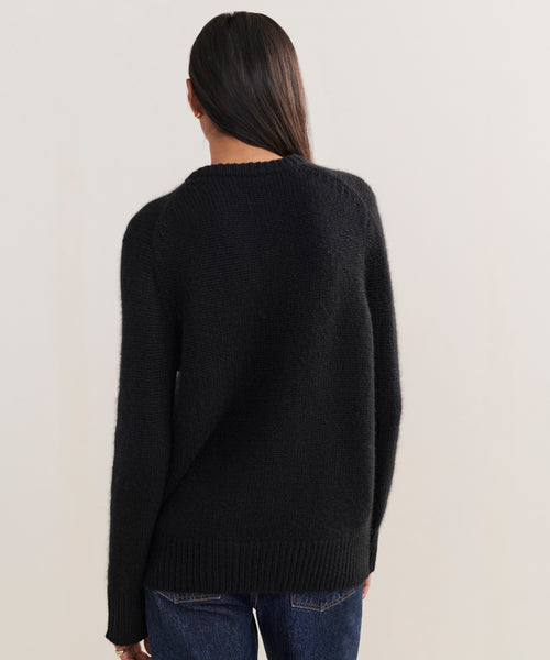 A person with long dark hair, wearing the Cashmere Kate V-Neck in black and relaxed-fit blue jeans, stands with their back to the camera against a plain light background.