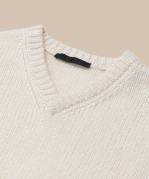 Close-up of the Cashmere Kate V-Neck sweater in ivory, featuring a ribbed collar and black neckline tag, set against a light beige background.