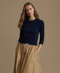 Woman wearing a navy Cashmere Leni Crewneck and beige skirt on a brown background