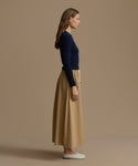 Woman wearing a navy Cashmere Leni Crewneck and beige skirt against a brown background