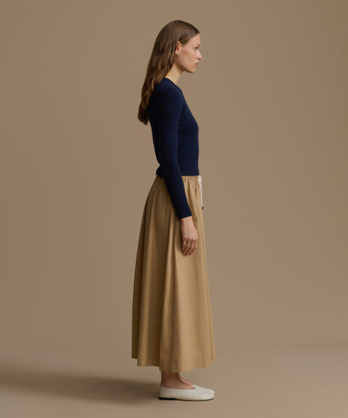 Woman wearing a navy Cashmere Leni Crewneck and beige skirt against a brown background