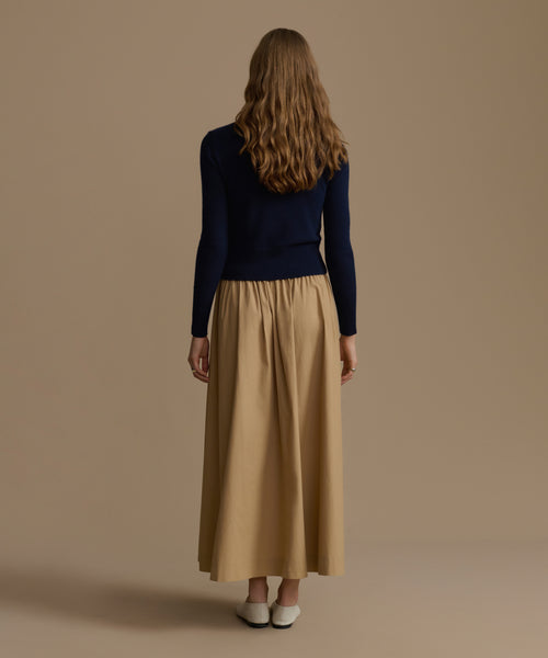 Woman wearing a navy Cashmere Leni Crewneck and beige skirt against a brown background