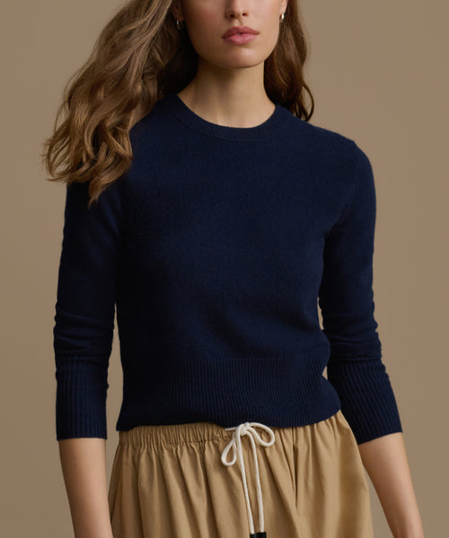 Woman wearing a navy Cashmere Leni Crewneck and beige pants against a brown background
