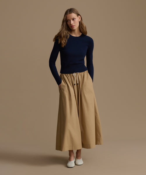 Woman wearing a Cashmere Leni Crewneck and beige wide-leg pants against a brown background