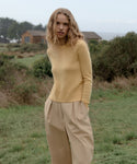 Woman in a yellow Cashmere Leni Crewneck and khaki trousers standing in a grassy field with a house in the background.