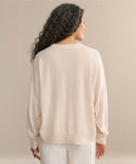 A woman with long, curly dark hair is shown from the back, wearing the Cashmere Marina Crewneck and white pants against a plain beige background.