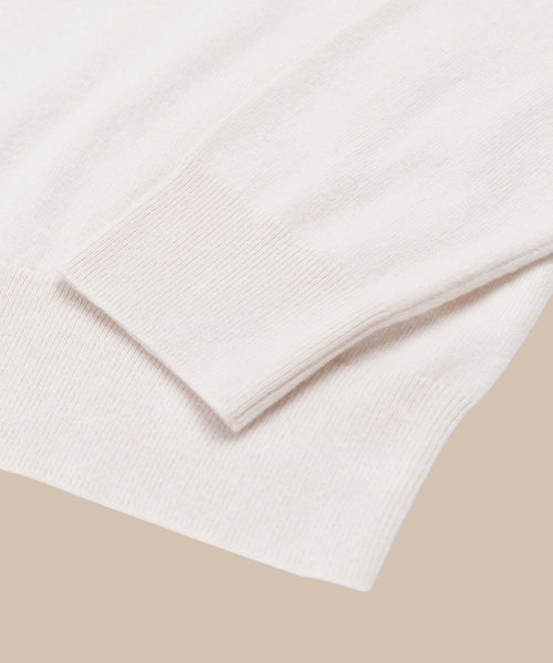A close-up of the Cashmere Marina Crewneck in light beige, showcasing its ribbed cuff and hem against a neutral background.