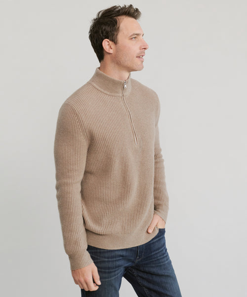 A man stands against a plain light background, wearing the Mens Wool Half Zip sweater in beige and dark blue jeans, his right hand in his pocket as he looks to the left.