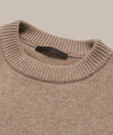 Close-up of the Cashmere Oversized Crewneck in beige, featuring a ribbed neckline and black label inside the collar, laid flat on a neutral background.