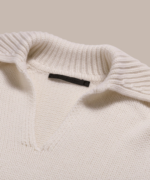 Close-up of the Cashmere Phoebe Polo in ivory, featuring a ribbed collar and V-shaped neckline in soft jersey-knit, laid on a neutral beige background.
