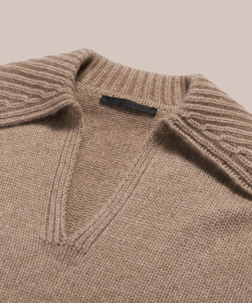 A close-up of the Cashmere Phoebe Polo—a women’s beige cashmere sweater with a wide ribbed collar and deep V-neck—laid flat on a light background.