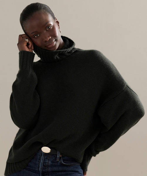 A person in the Cashmere Porter Turtleneck and blue jeans stands relaxed, one hand on their head and the other in their pocket, set against a neutral background.