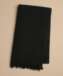 A folded black Cashmere Shawl with fringed ends rests on a plain beige background.