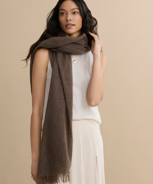 A woman with long dark hair wears a sleeveless white top and cream skirt, accessorized with a Cashmere Shawl draped around her neck. She stands against a plain beige background.