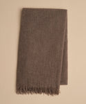 A folded brown Cashmere Shawl with short fringes at one end, crafted from soft, lightweight cashmere, rests on a beige surface.