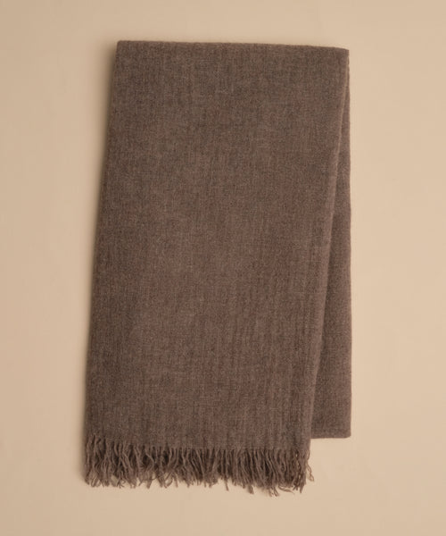 A folded brown Cashmere Shawl with short fringes at one end, crafted from soft, lightweight cashmere, rests on a beige surface.