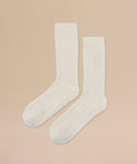 A pair of Cashmere Socks in ivory with a ribbed crew design, perfect for fall and winter, laid flat on a beige background with toes pointing to the lower left corner.
