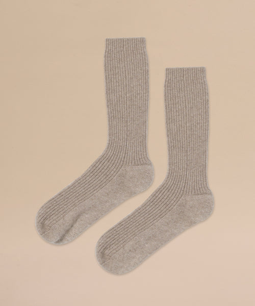 A pair of Cashmere Socks in light gray ribbed knit are laid flat side by side on a beige background.