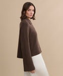 A woman with shoulder-length brown hair wears the Cashmere Stevie Polo and a white skirt, standing against a beige background and looking toward the camera.
